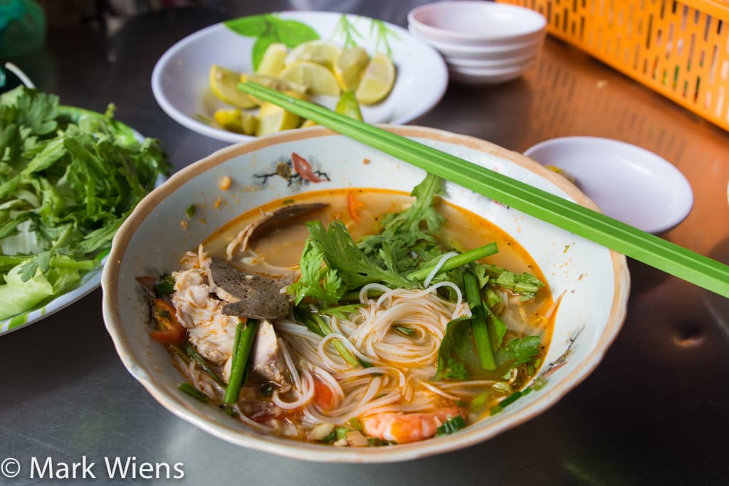 Street vendor in Cholon ladling clear broth into a bowl of hu tieu nam vang at a morning food stall